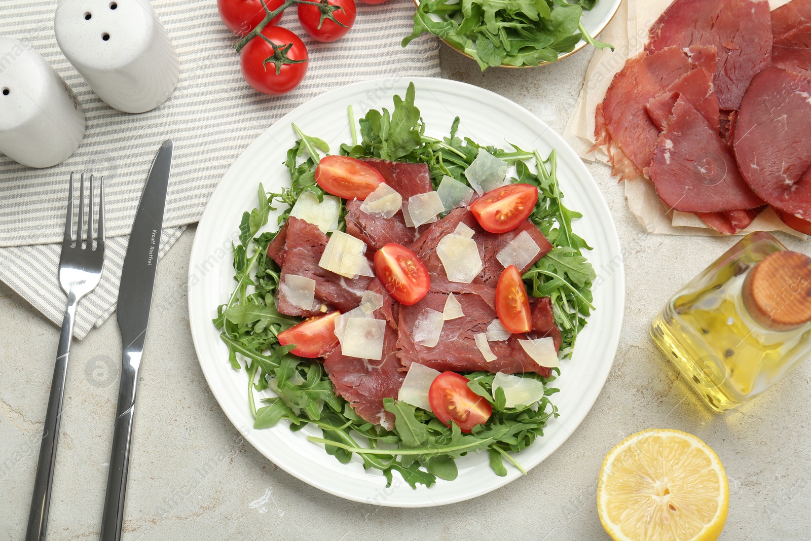 Photo of Flat lay composition with delicious bresaola salad on light grey textured table