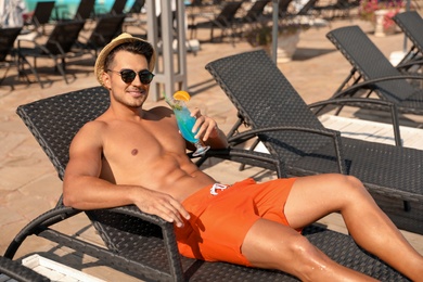Young man with cocktail on lounge chair near outdoor pool