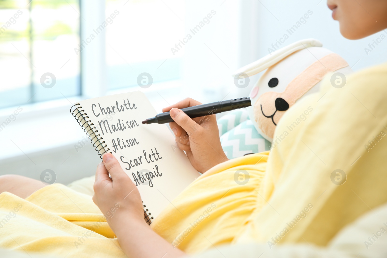 Photo of Pregnant woman with baby names list sitting in armchair, closeup