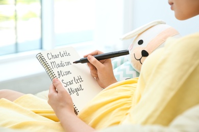 Photo of Pregnant woman with baby names list sitting in armchair, closeup