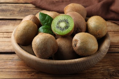 Bowl with cut and whole fresh kiwis on wooden table