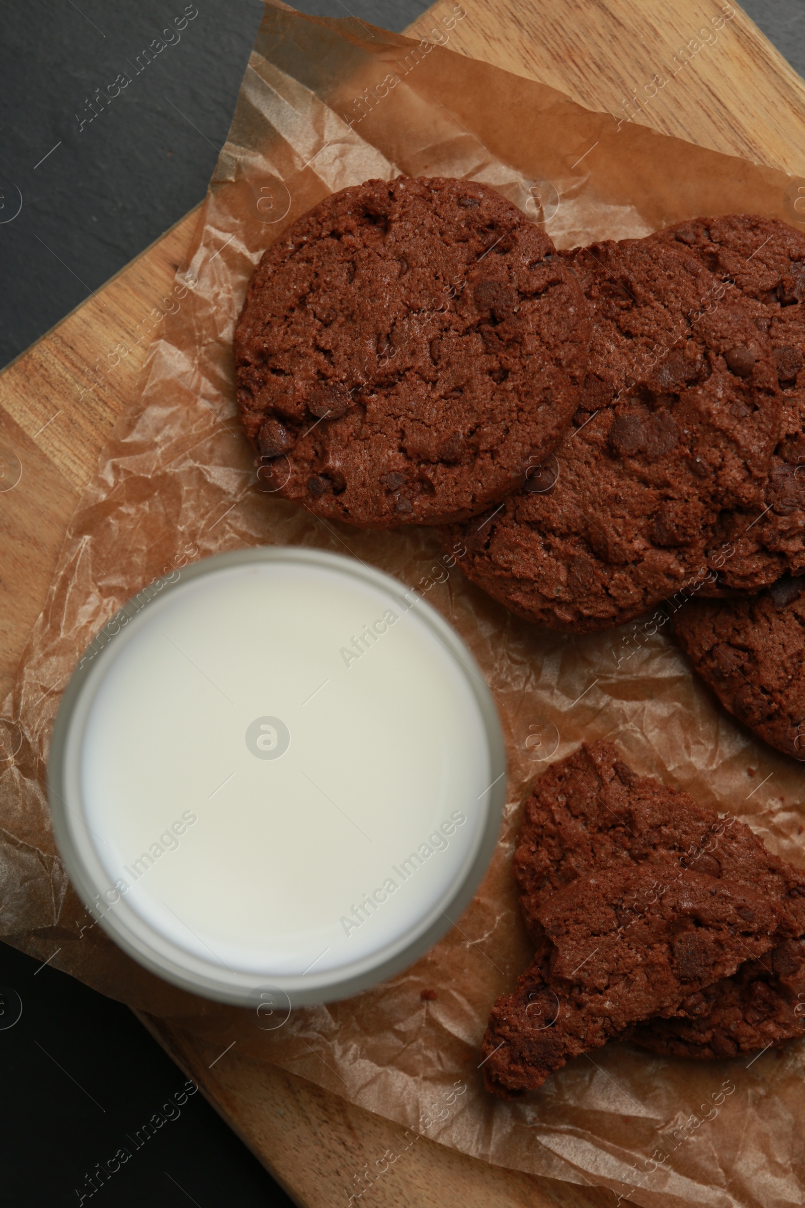 Photo of Board with tasty chocolate cookies and glass of milk on dark table, top view