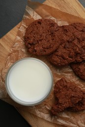 Board with tasty chocolate cookies and glass of milk on dark table, top view