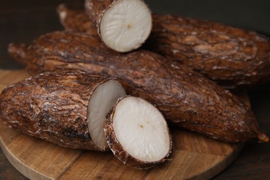 Photo of Whole and cut cassava roots on wooden table, closeup