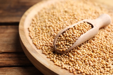 Mustard seeds and scoop in bowl on wooden table, closeup