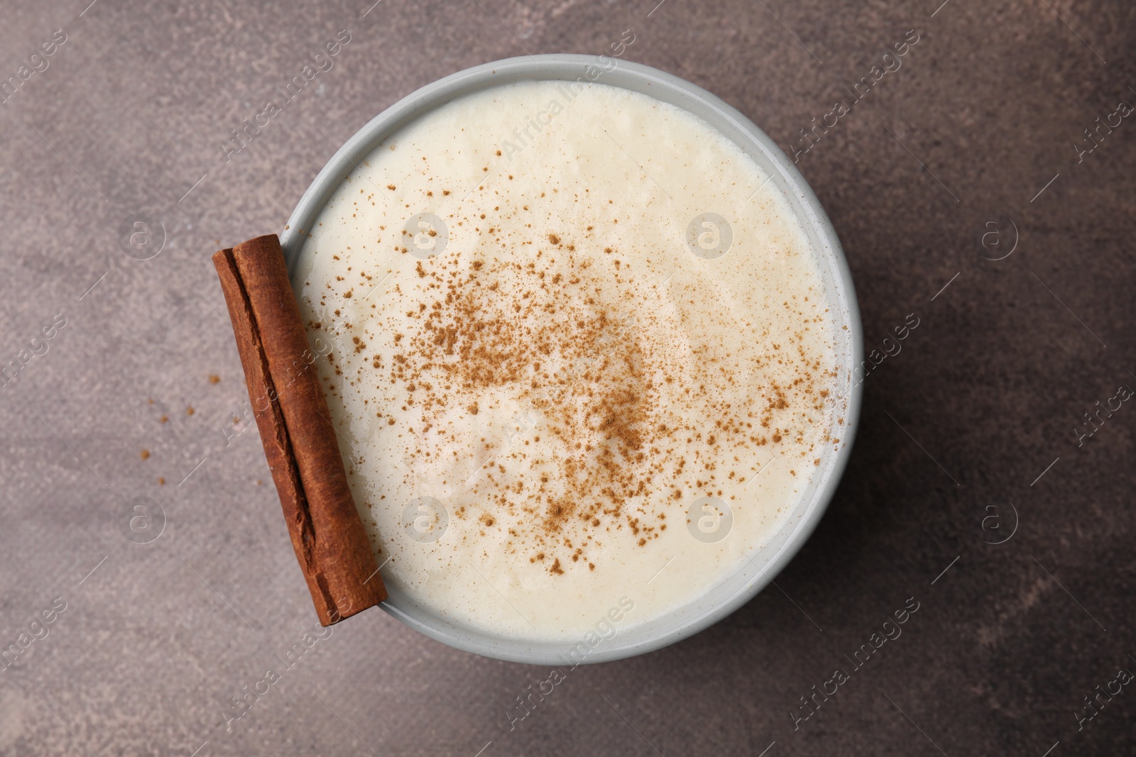 Photo of Delicious semolina pudding with cinnamon in bowl on brown table, top view