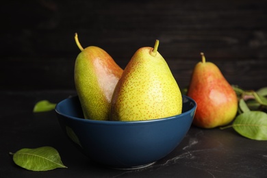 Photo of Bowl with ripe juicy pears on black stone table against dark background