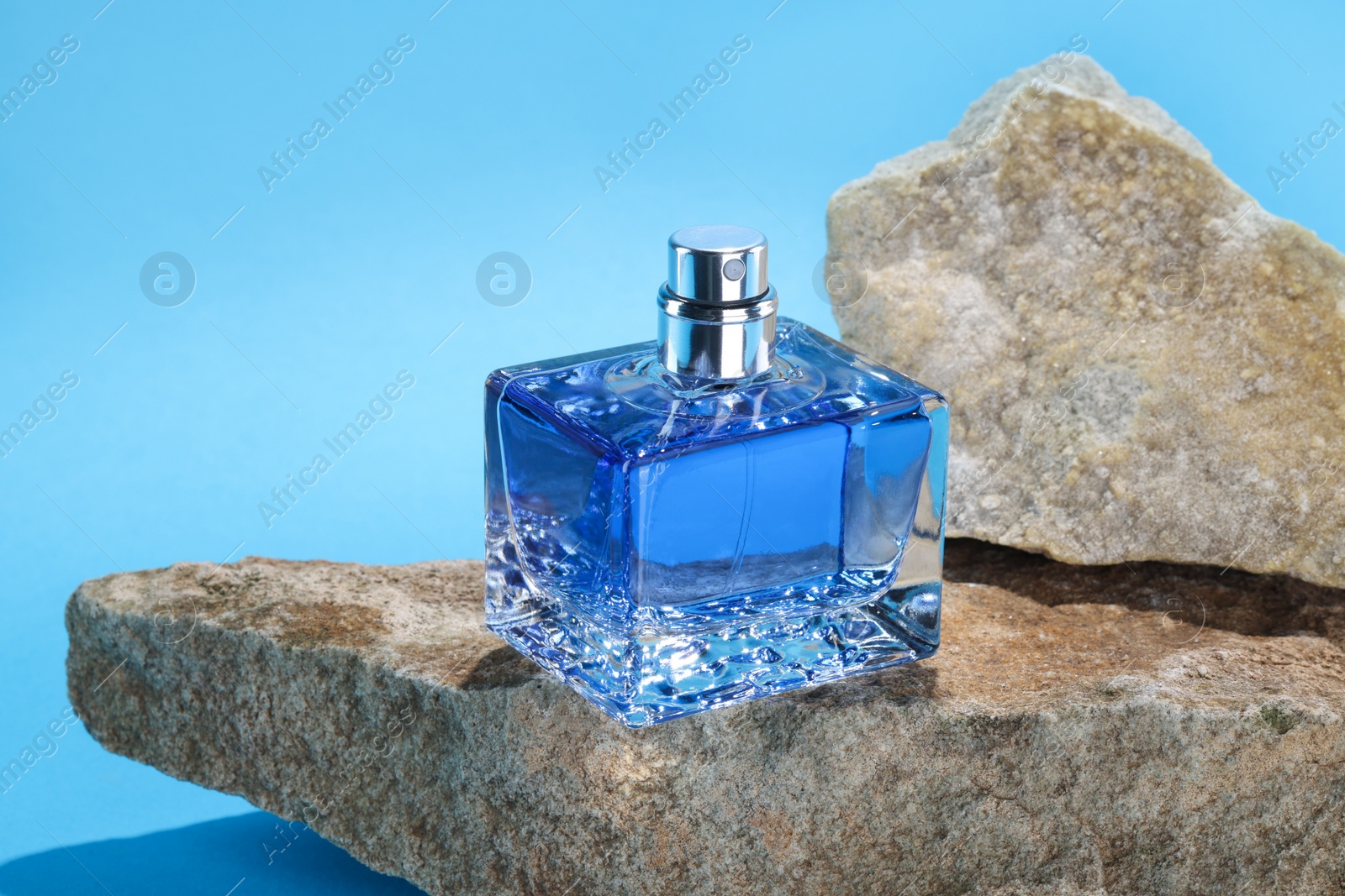 Photo of Stylish presentation of luxury men`s perfume on stones against light blue background