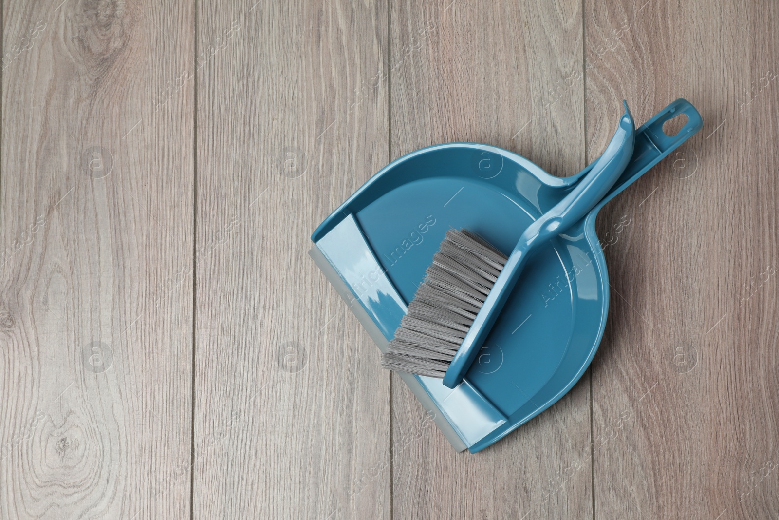 Photo of Plastic whisk broom with dustpan on wooden floor, top view. Space for text