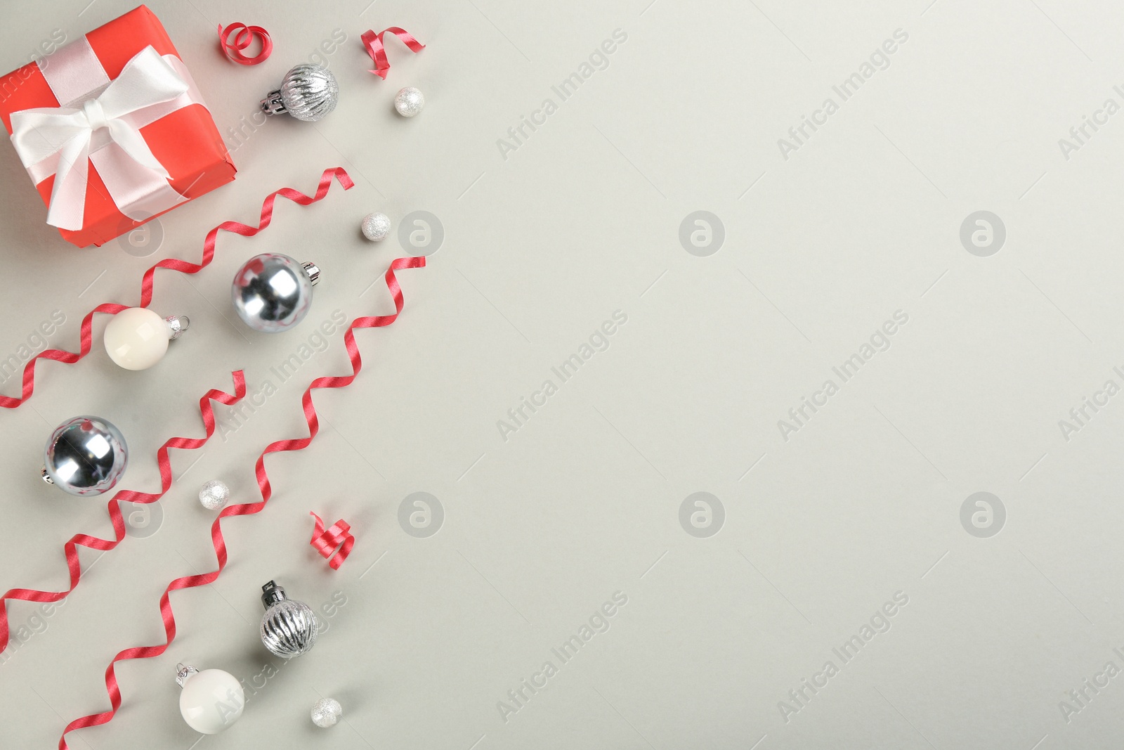 Photo of Red serpentine streamers, Christmas balls and gift box on light grey background, flat lay. Space for text