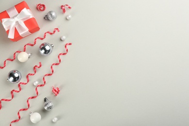 Red serpentine streamers, Christmas balls and gift box on light grey background, flat lay. Space for text