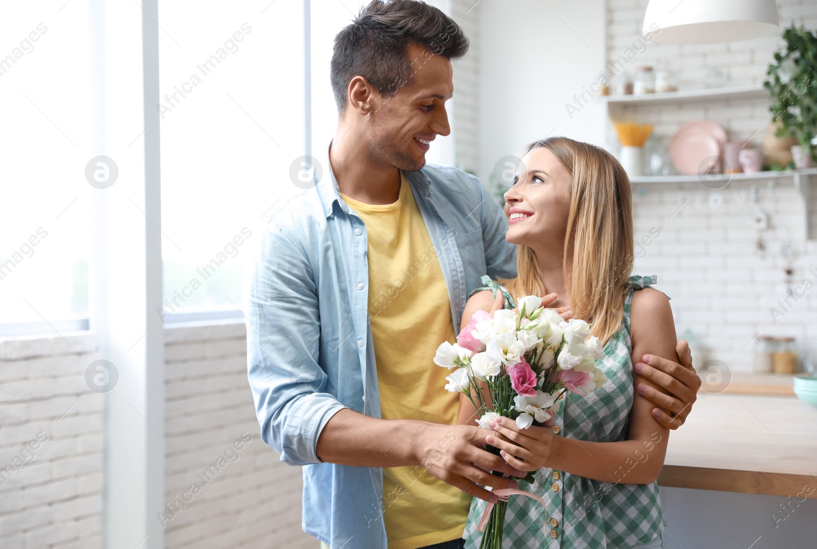 Photo of Young man with flowers bouquet congratulating his girlfriend in kitchen, space for text
