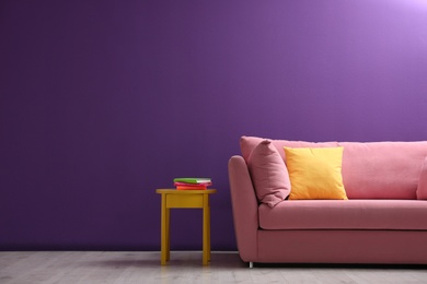 Photo of Comfortable pink sofa near purple wall in living room interior
