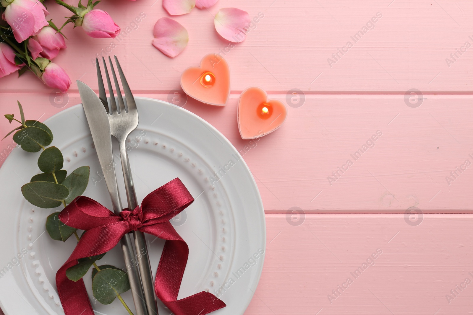 Photo of Place setting with heart shaped candles and bouquet of roses for romantic dinner on pink wooden table, flat lay. Space for text