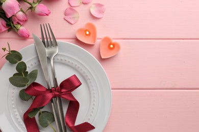 Place setting with heart shaped candles and bouquet of roses for romantic dinner on pink wooden table, flat lay. Space for text