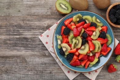 Plate of delicious fresh fruit salad and ingredients on wooden table, flat lay. Space for text