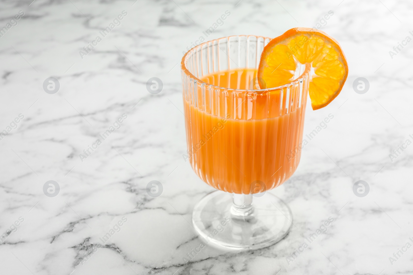 Photo of Delicious tangerine liqueur in glass on white marble table, closeup. Space for text