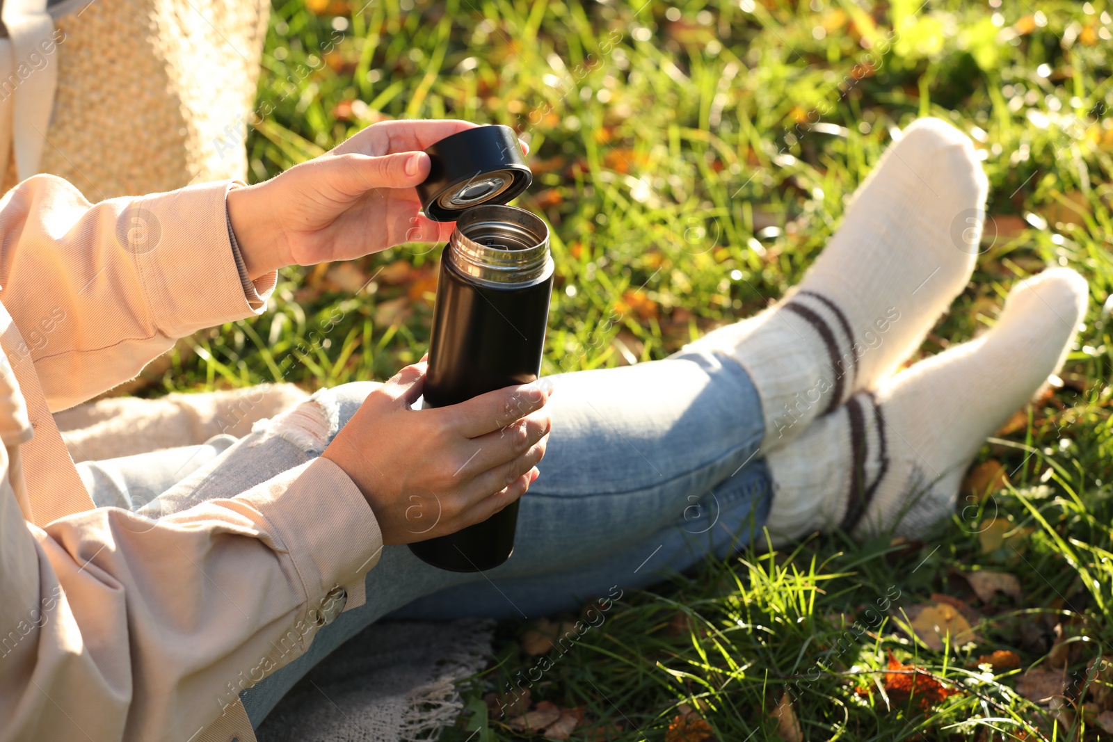 Photo of Woman opening thermos on green grass outdoors, closeup