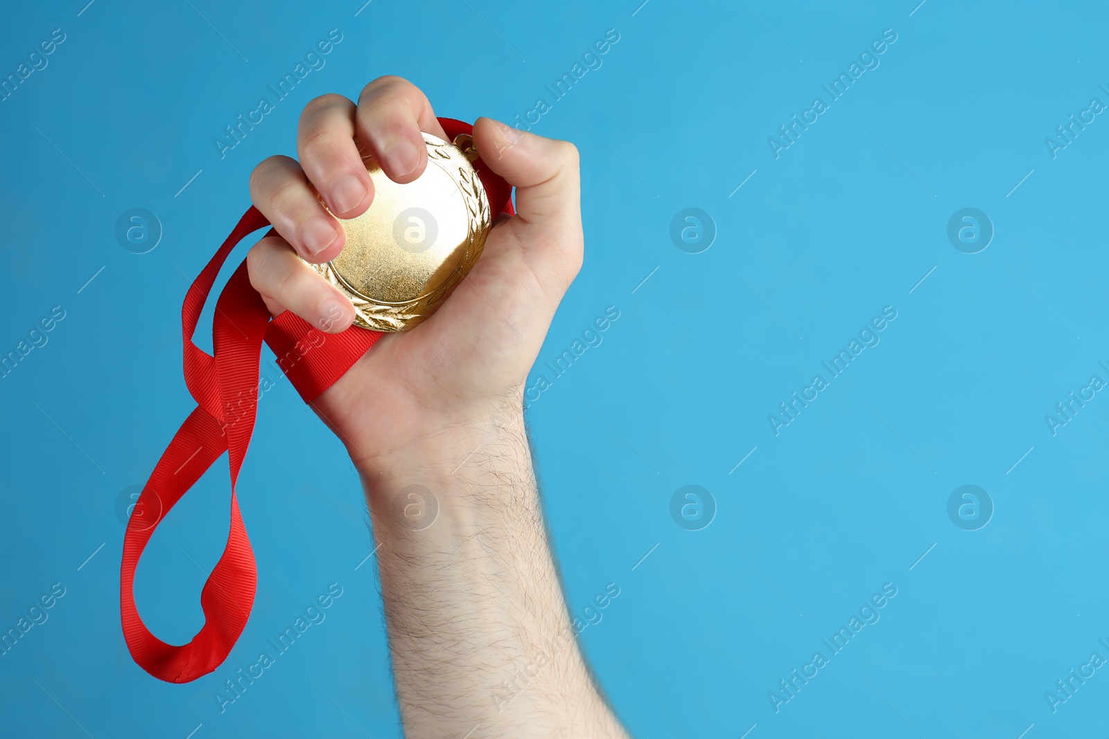 Photo of Man holding golden medal on blue background, closeup. Space for design