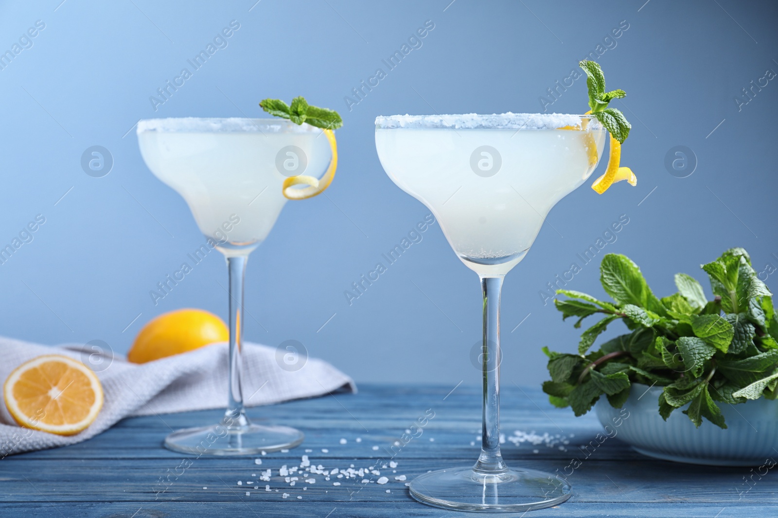 Photo of Glasses of tasty Margarita cocktail on blue wooden table