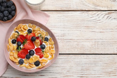 Photo of Bowl of tasty crispy corn flakes with milk and berries on white wooden table, flat lay. Space for text