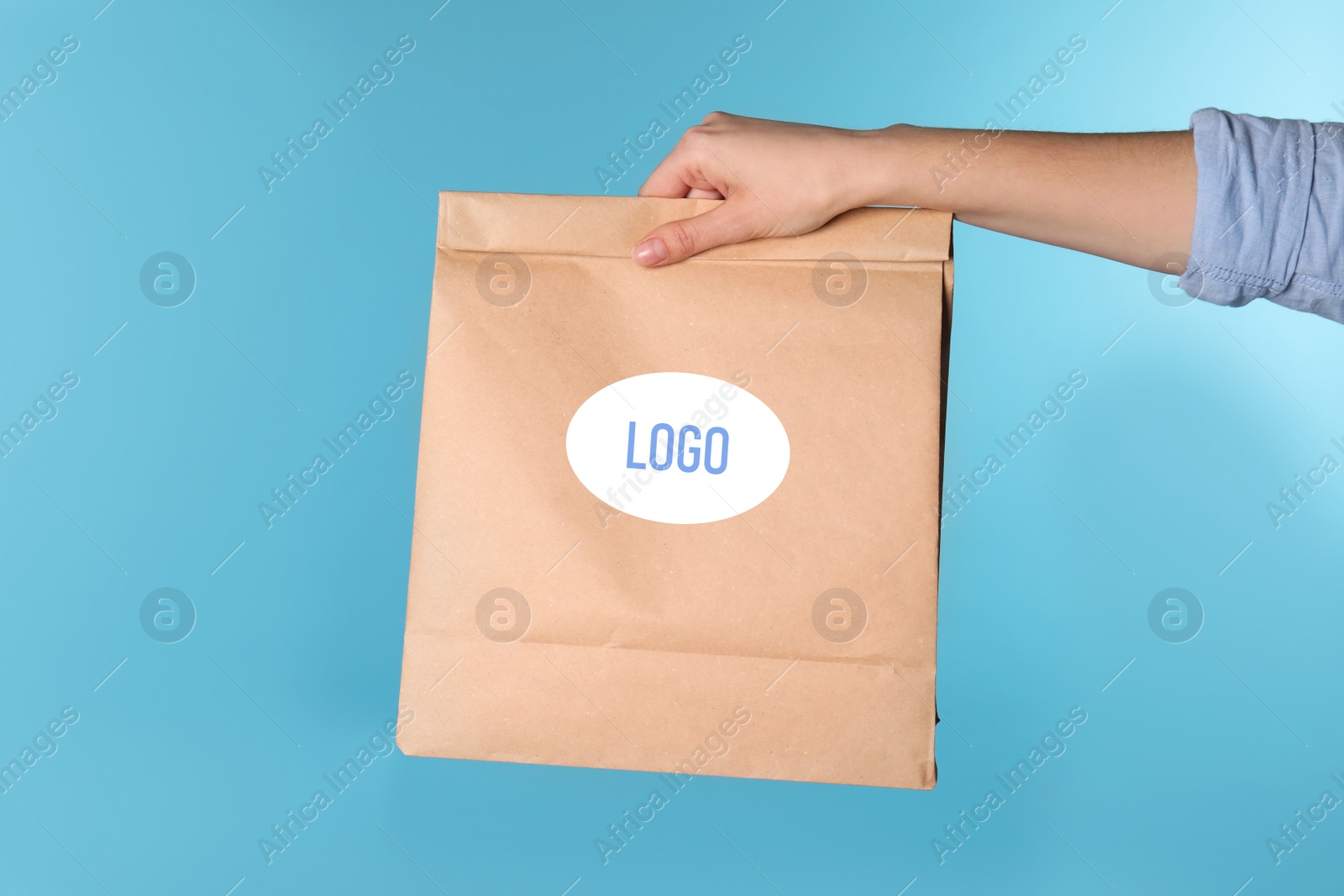 Image of Woman holding paper bag with with logo on light blue background, closeup