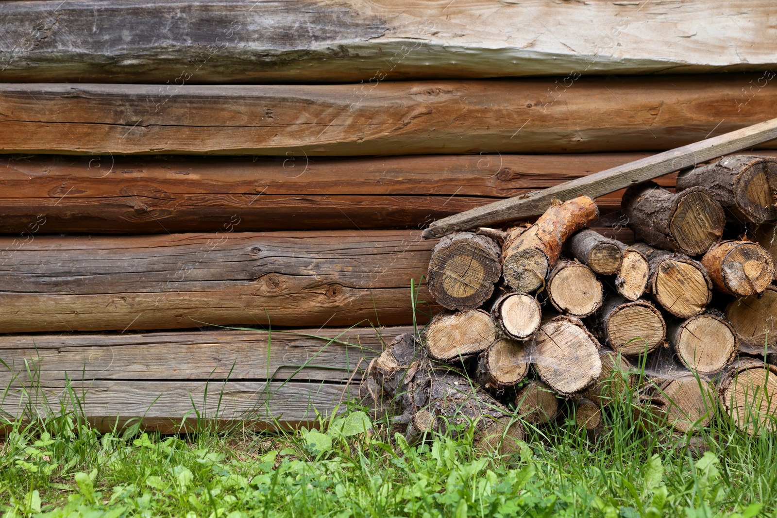 Photo of Pile of cut firewood near wooden wall on summer day, space for text