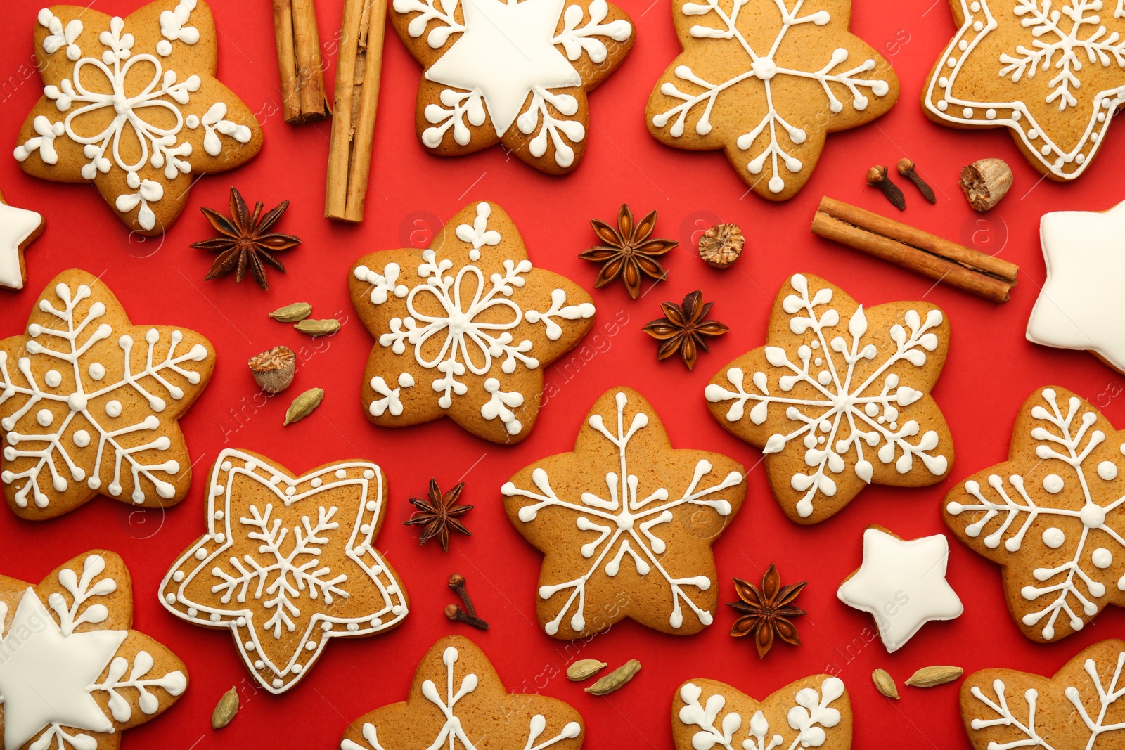 Photo of Tasty star shaped Christmas cookies with icing and spices on red background, flat lay