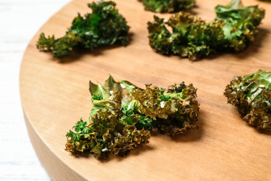 Photo of Tasty baked kale chips on wooden board, closeup