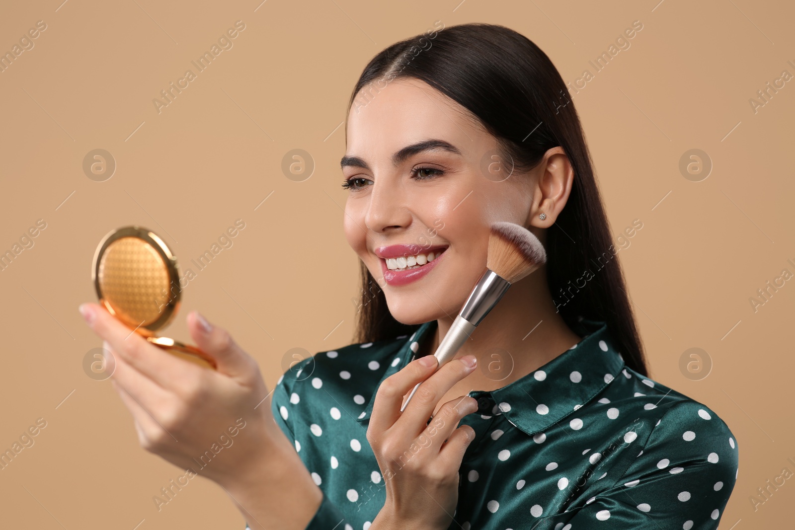 Photo of Happy woman with cosmetic pocket mirror applying makeup on light brown background