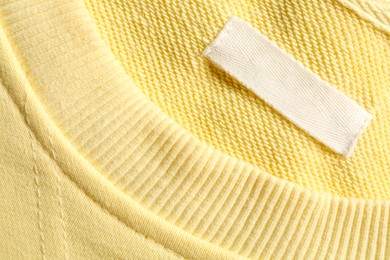 Photo of Blank clothing label on yellow sweater, top view. Space for text