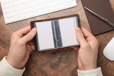 Man holding leather business card holder with blank cards at wooden table, top view