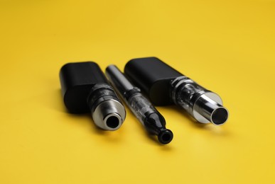 Different reusable electronic cigarettes on yellow background, closeup