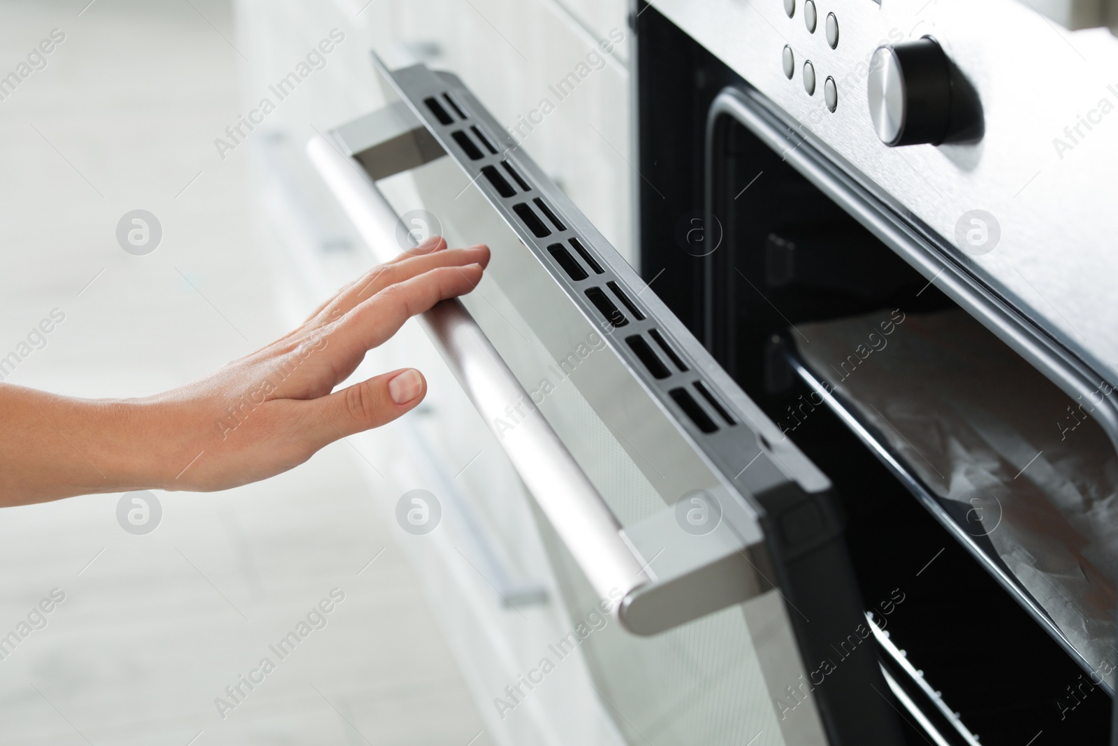 Photo of Young woman opening electric oven in kitchen, closeup