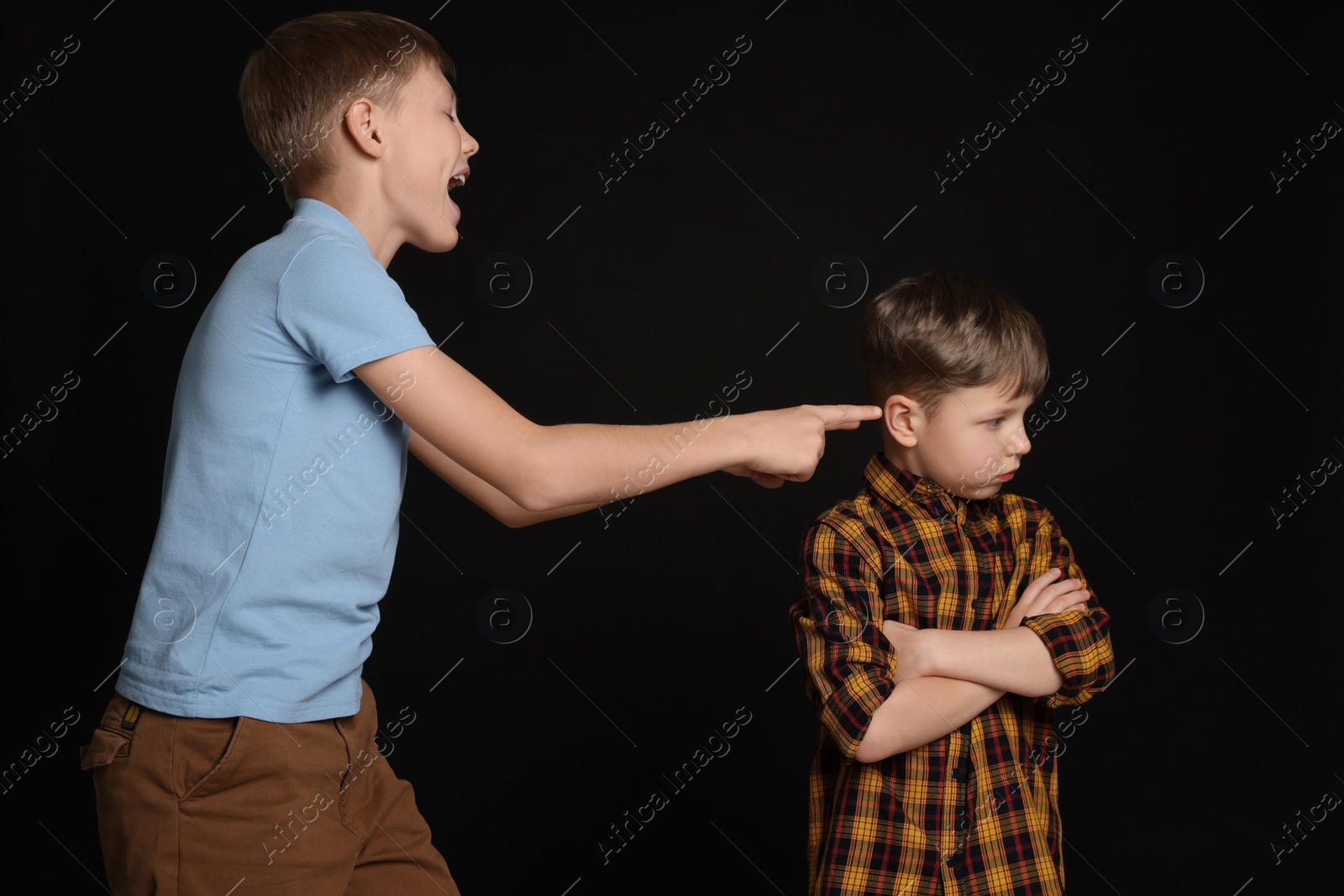 Photo of Boy laughing and pointing at upset kid on black background. Children's bullying