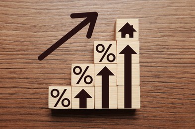 Image of Mortgage rate rising illustrated by upward arrows, cubes with percent signs and house icon on wooden background, flat lay