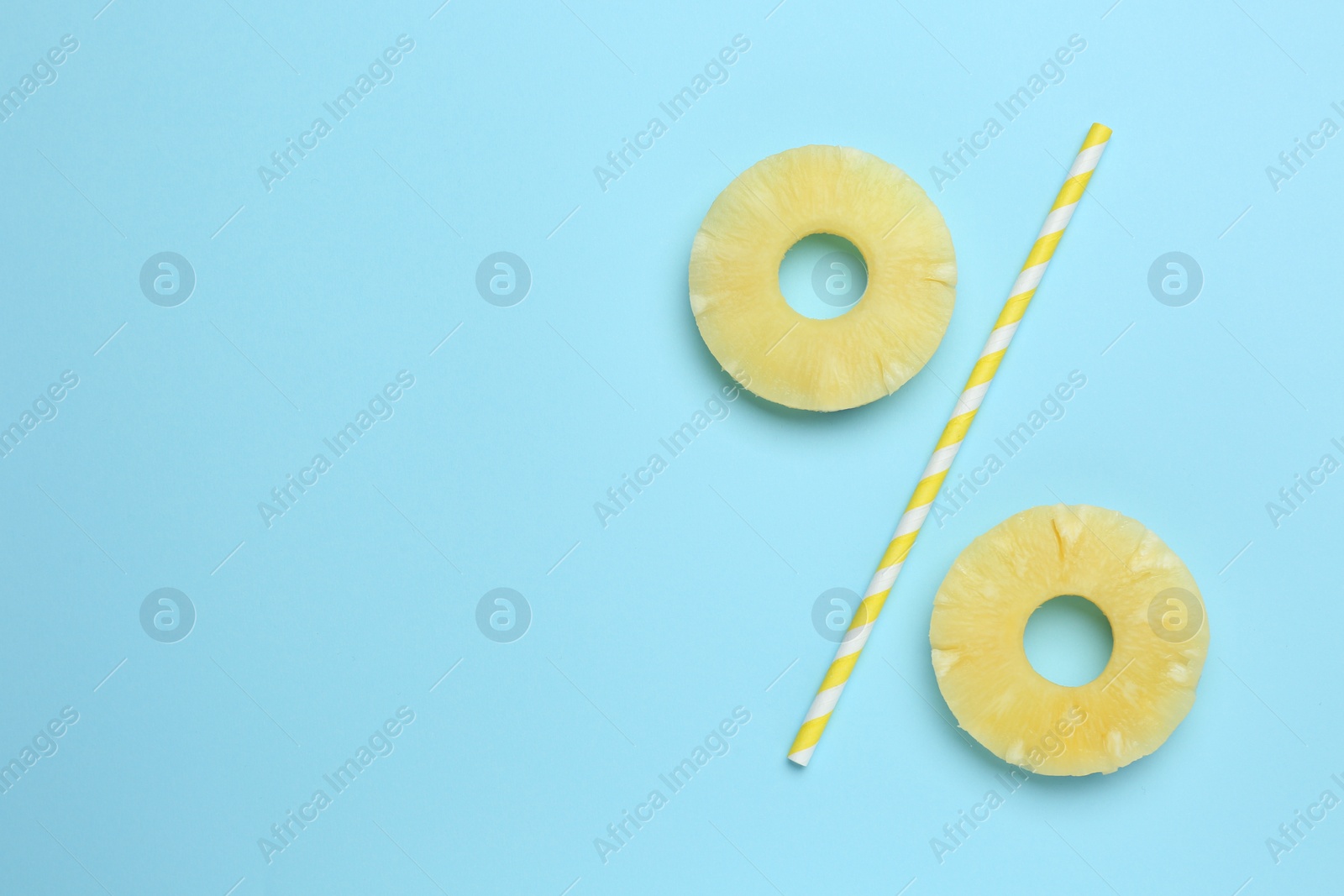 Photo of Percent sign made of pineapple rings and straw on light blue background, flat lay. Space for text