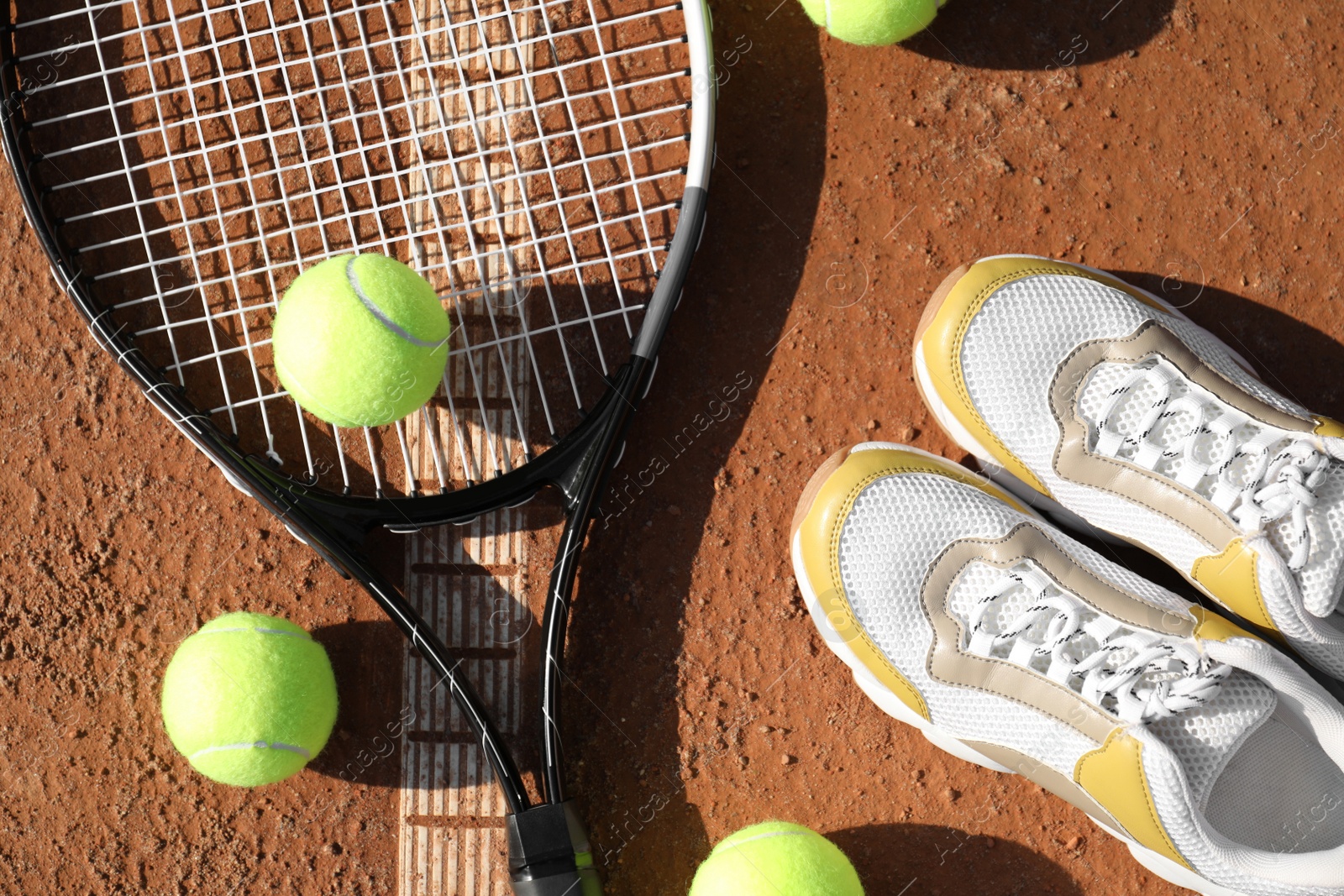 Photo of Tennis balls, racket and shoes on clay court, flat lay