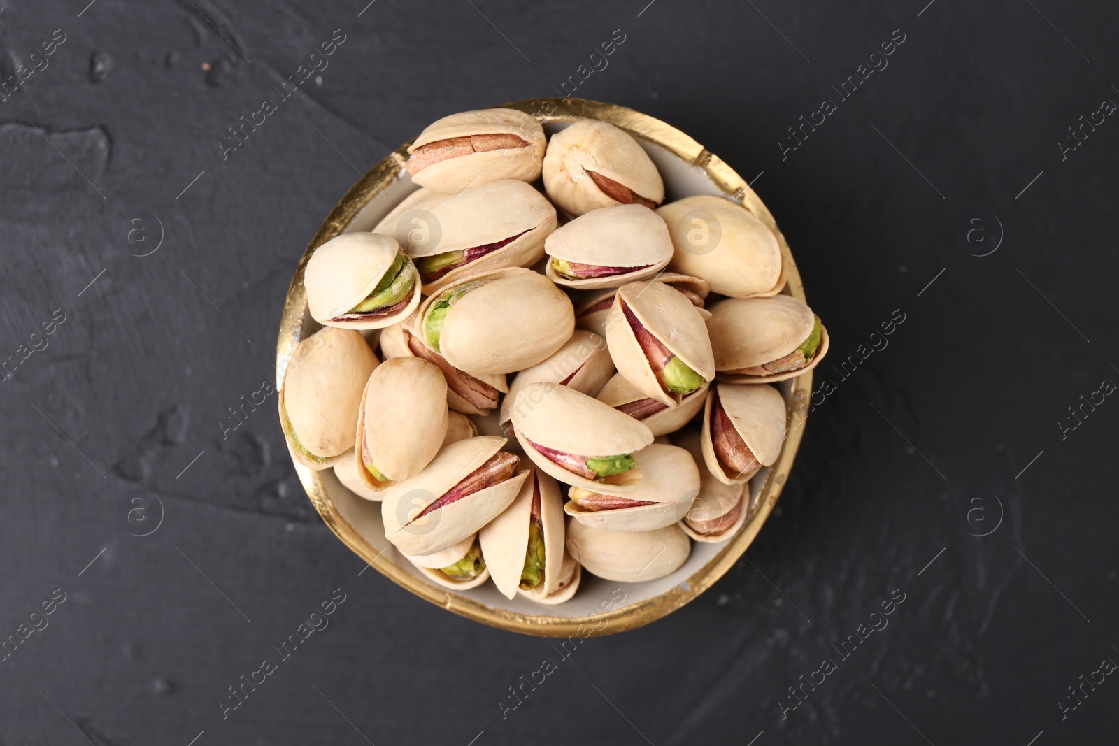 Photo of Tasty pistachios in bowl on black table, top view
