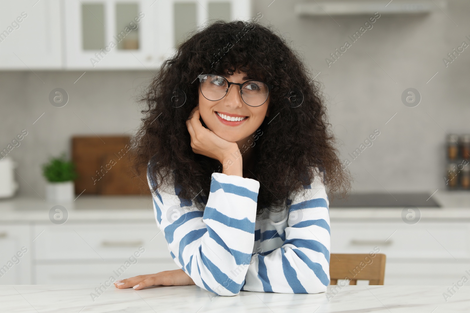 Photo of Portrait of beautiful woman with curly hair in kitchen. Attractive lady smiling and posing for camera