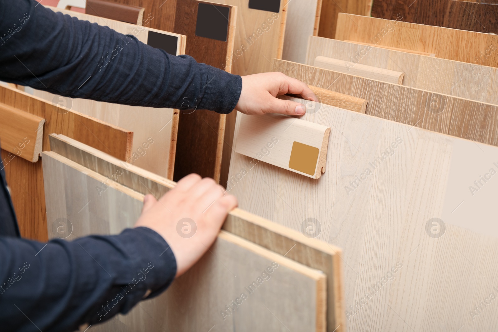 Photo of Man choosing wooden flooring among different samples in shop, closeup