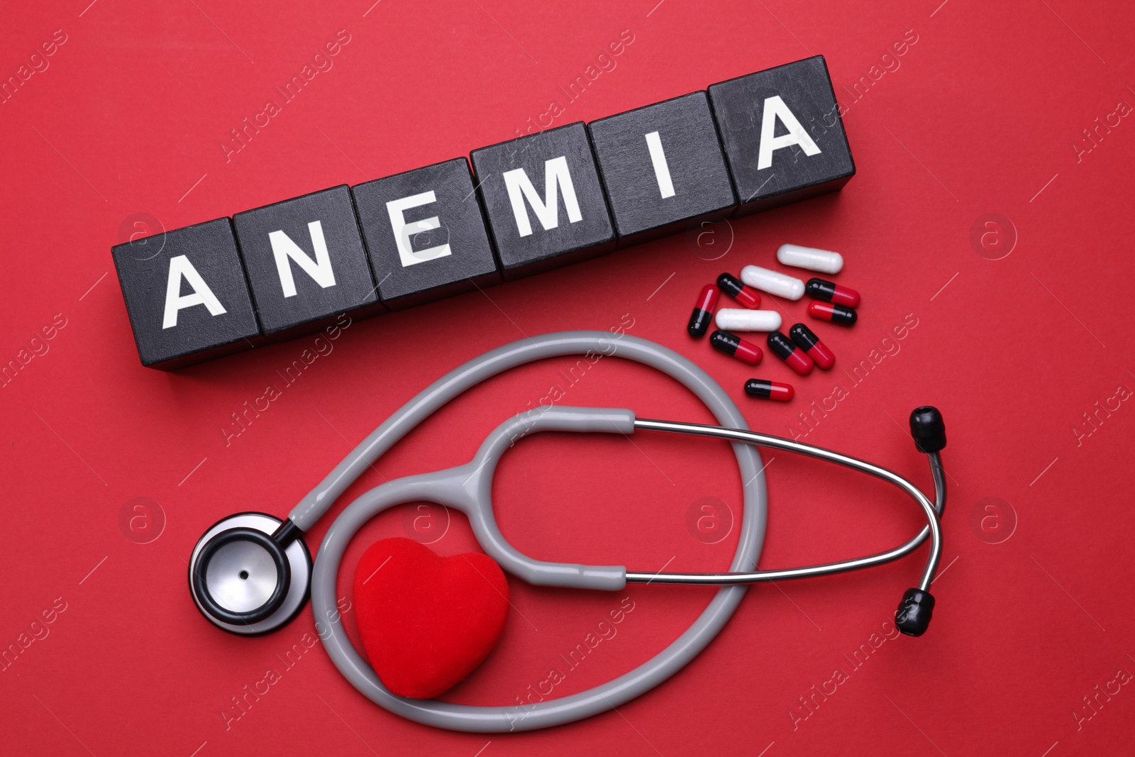 Photo of Word Anemia made with black wooden cubes, pills, stethoscope and decorative heart on red background, flat lay