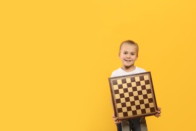 Photo of Cute girl holding chessboard on orange background. Space for text