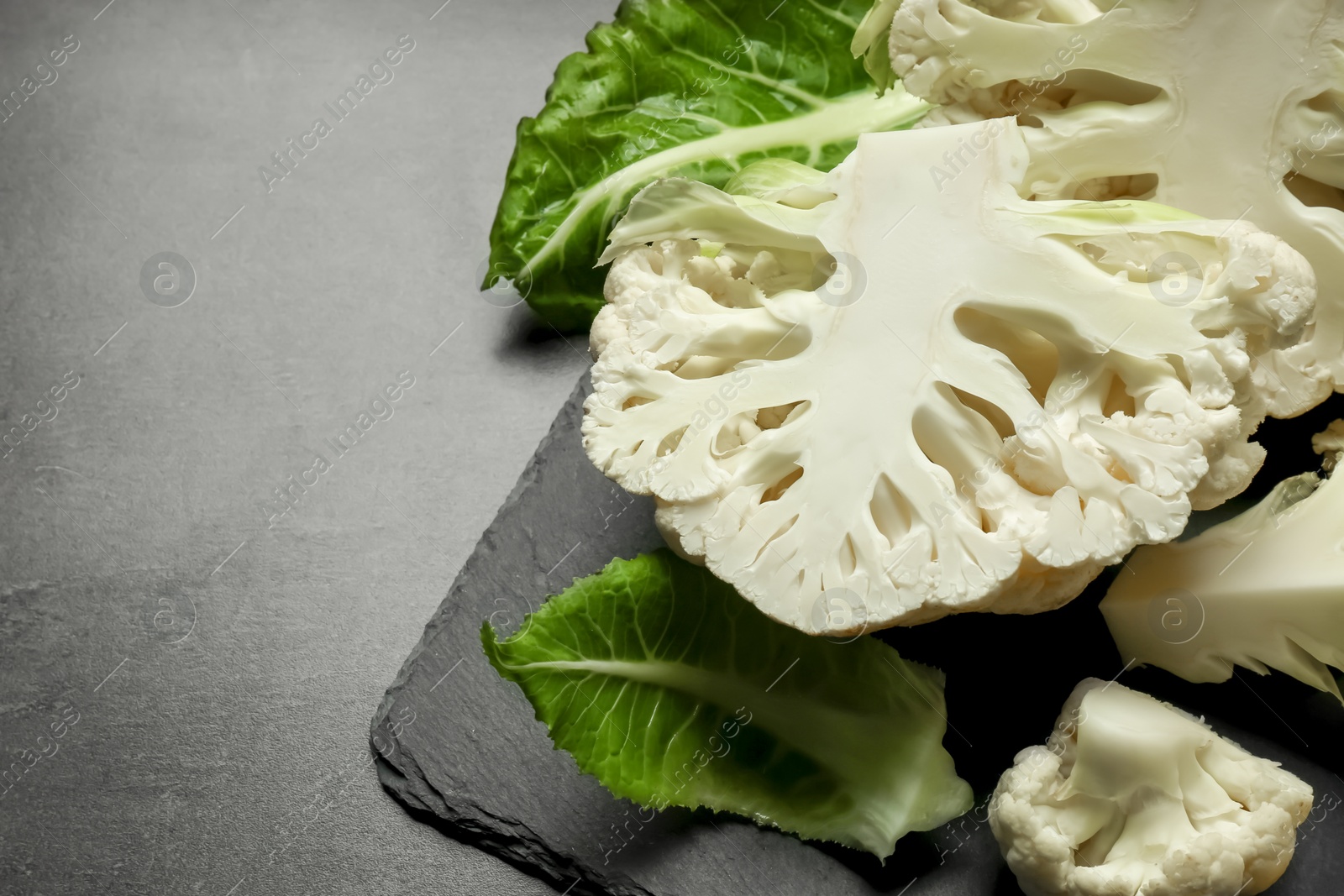 Photo of Cut fresh raw cauliflowers on black table. Space for text