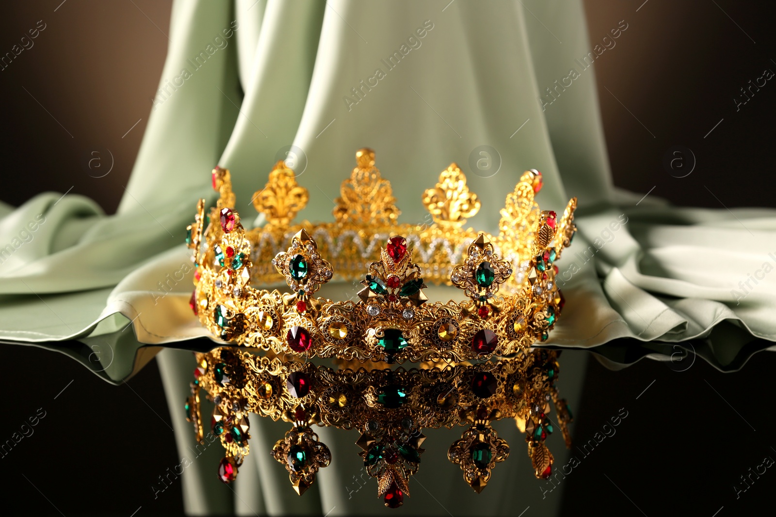 Photo of Beautiful golden crown with gems near light cloth on black table