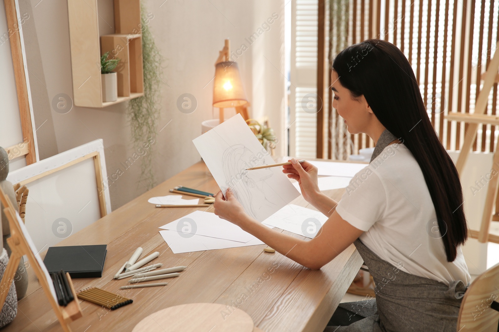 Photo of Young woman drawing female portrait at table indoors