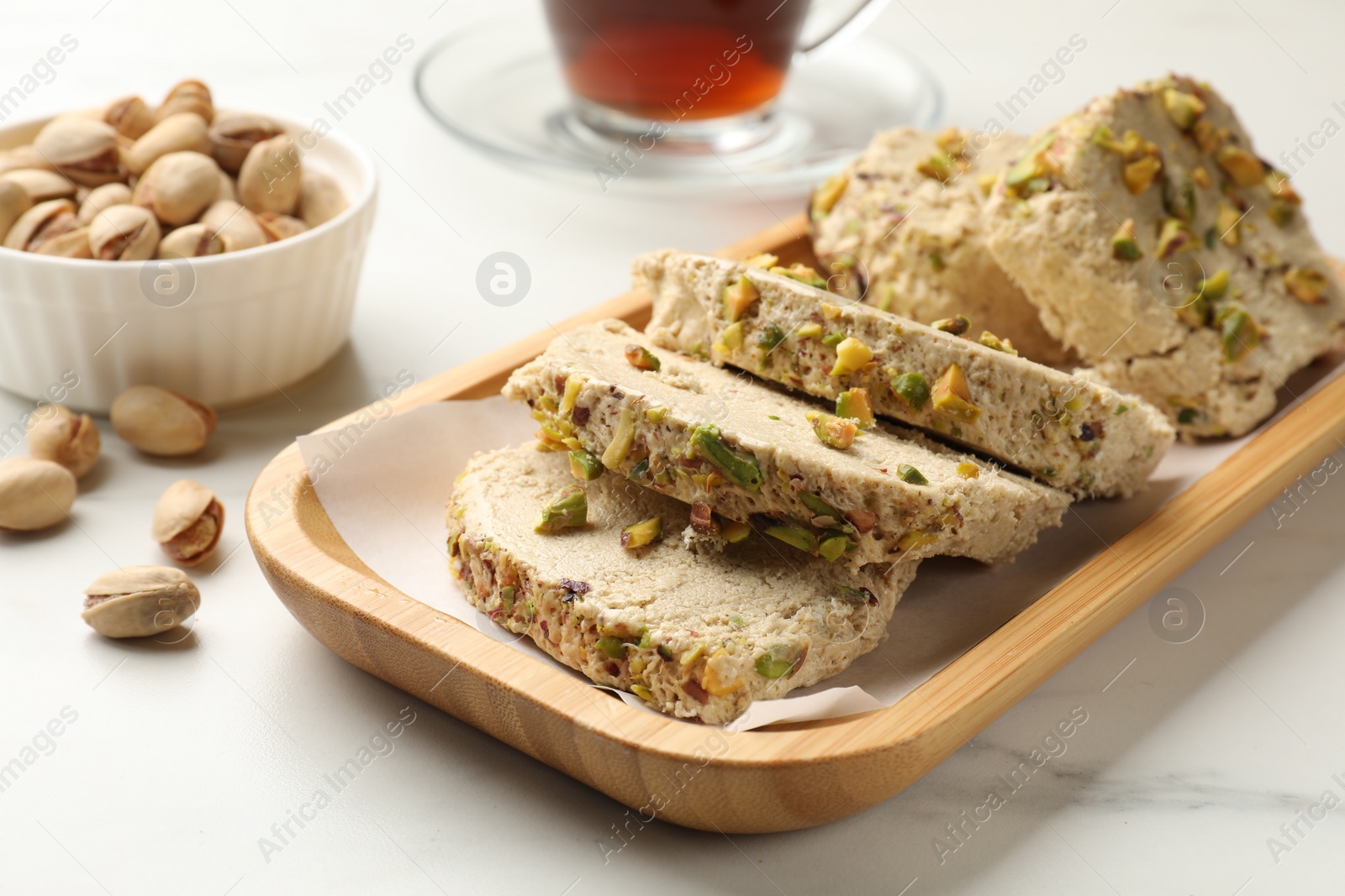 Photo of Tasty halva with pistachios on white marble table, closeup