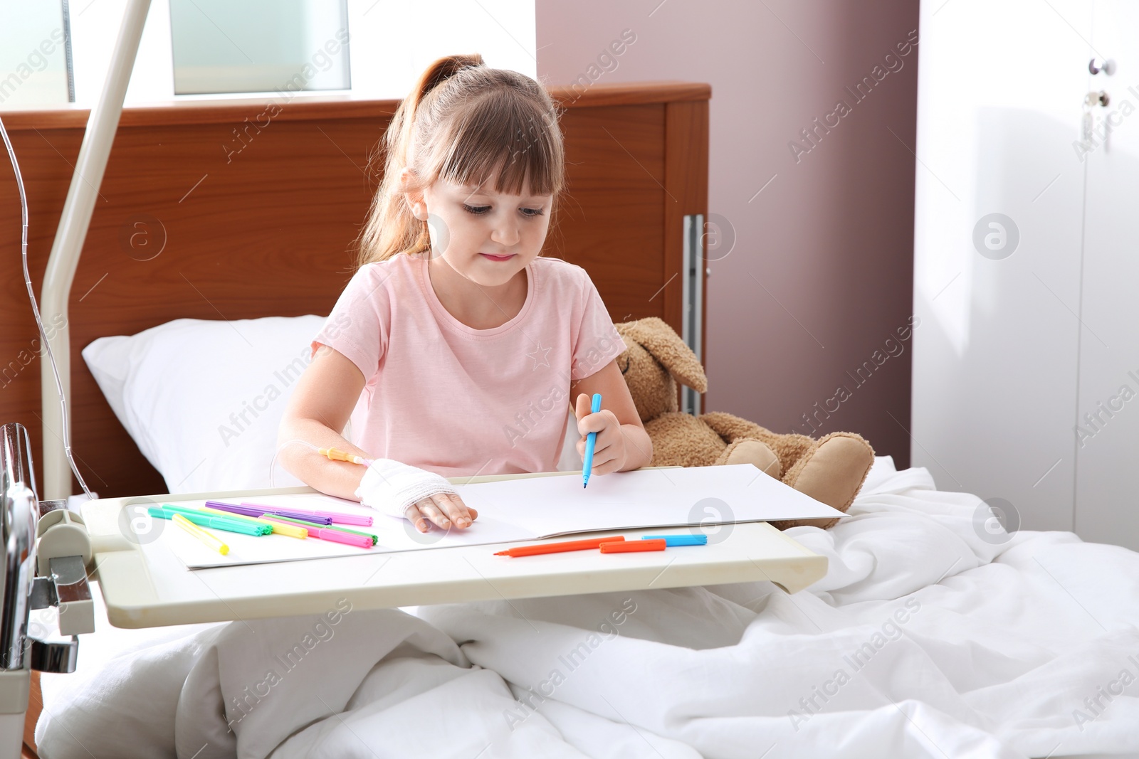 Photo of Little child with intravenous drip drawing in hospital bed