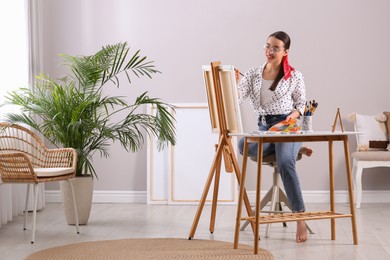 Photo of Happy woman artist drawing picture on canvas in studio