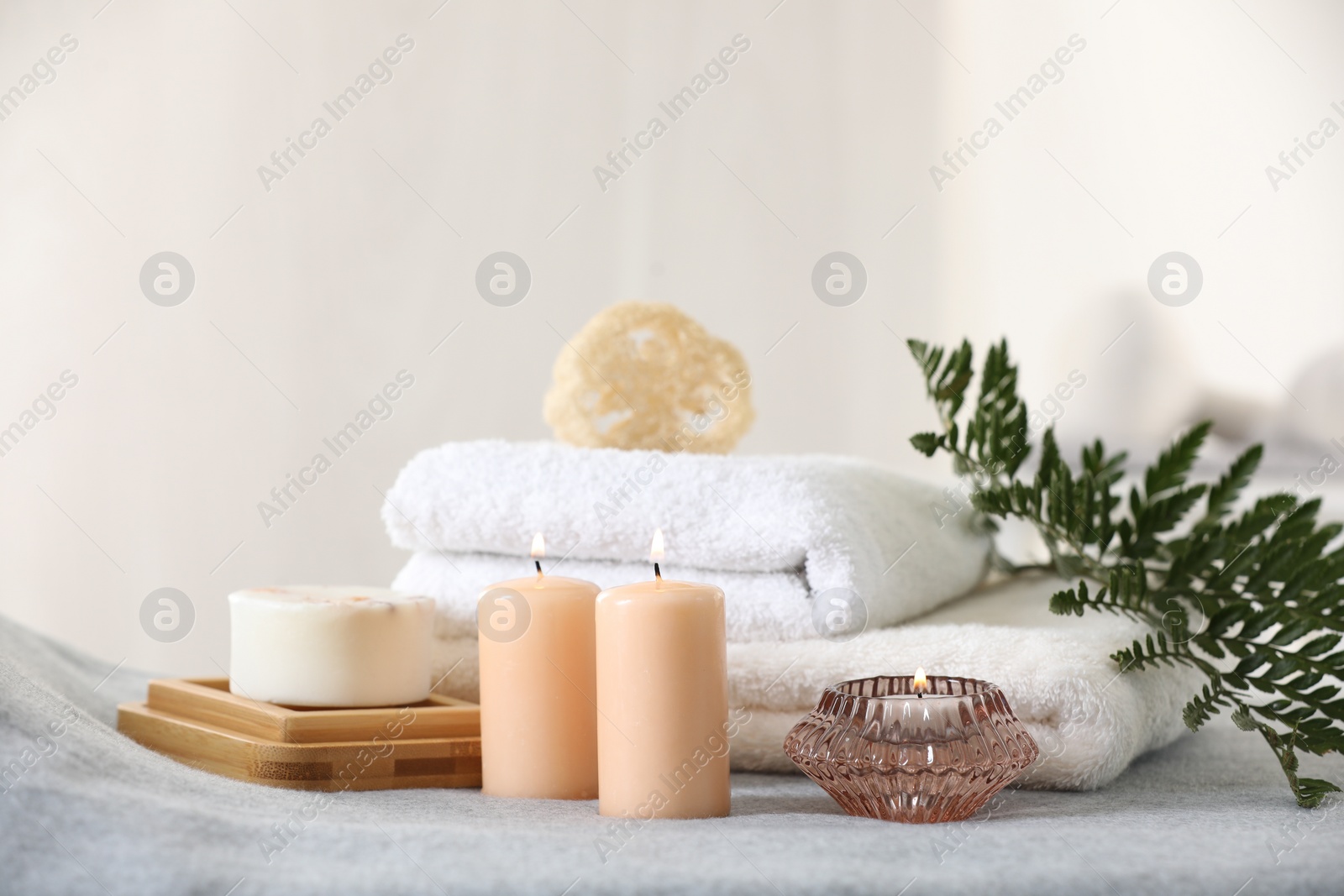 Photo of Spa composition. Burning candles, soap, towels and loofah on soft grey surface